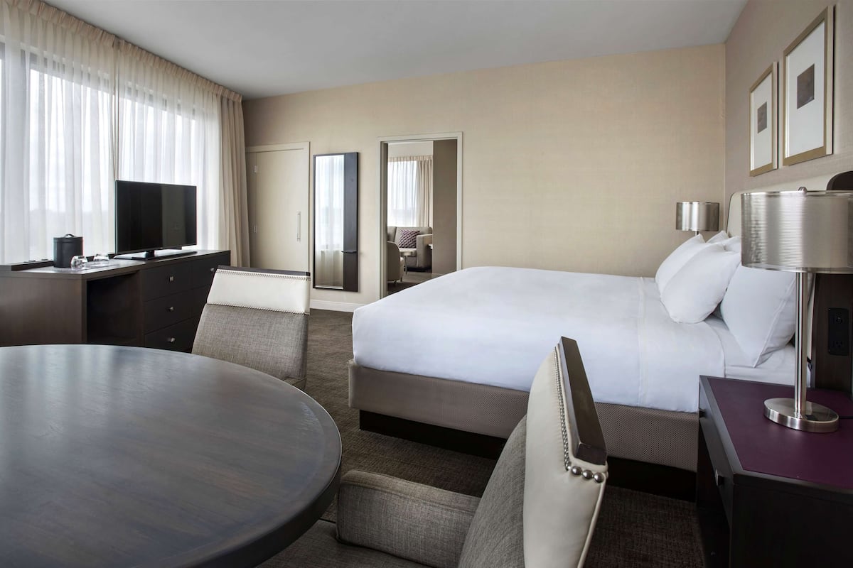 A hotel room with a bed, a desk, a chair, a round table, a television, and a lamp.