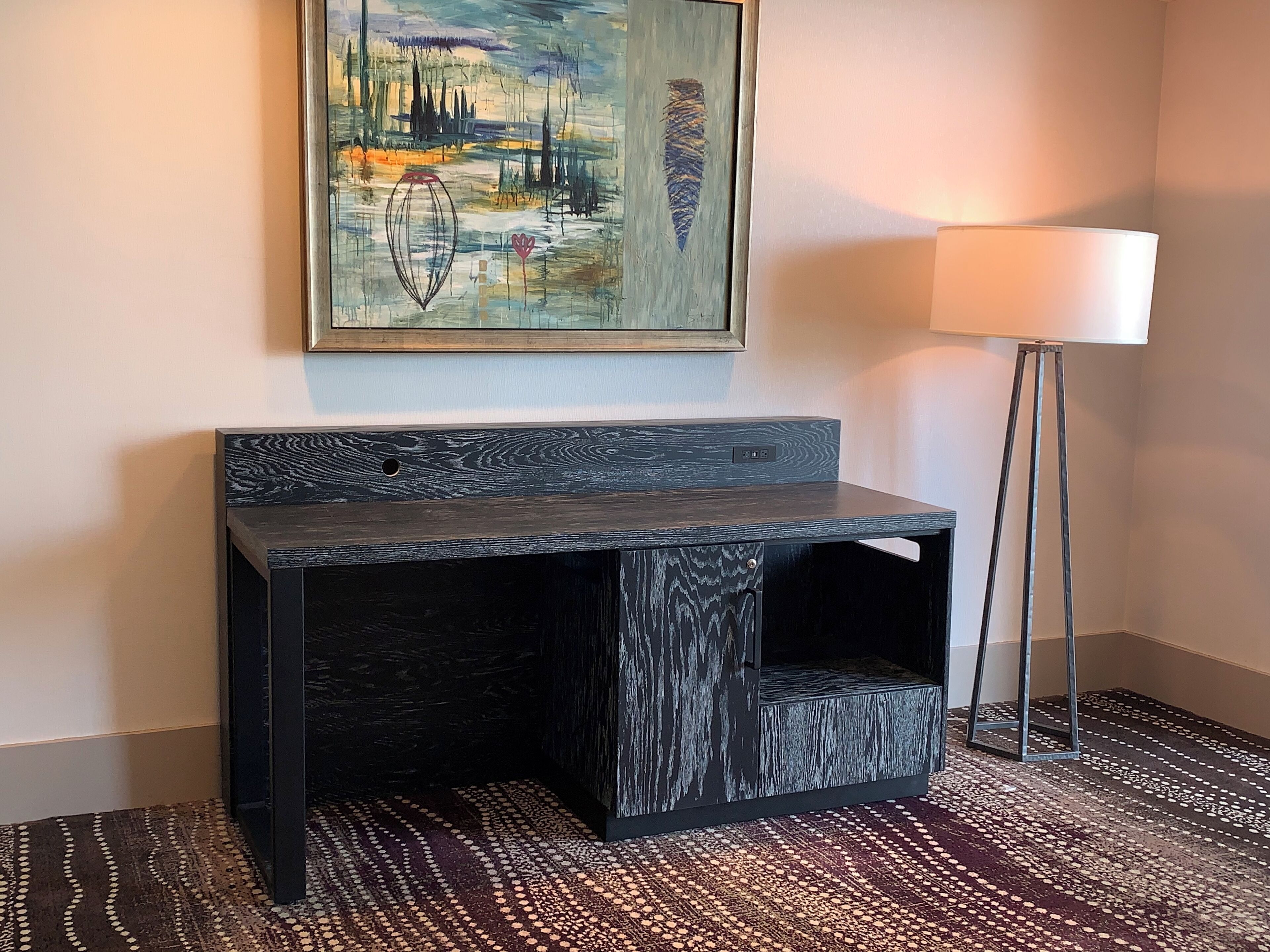 A modern, dark wood console table with a built-in bench, a painting above it, and a floor lamp to the right.
