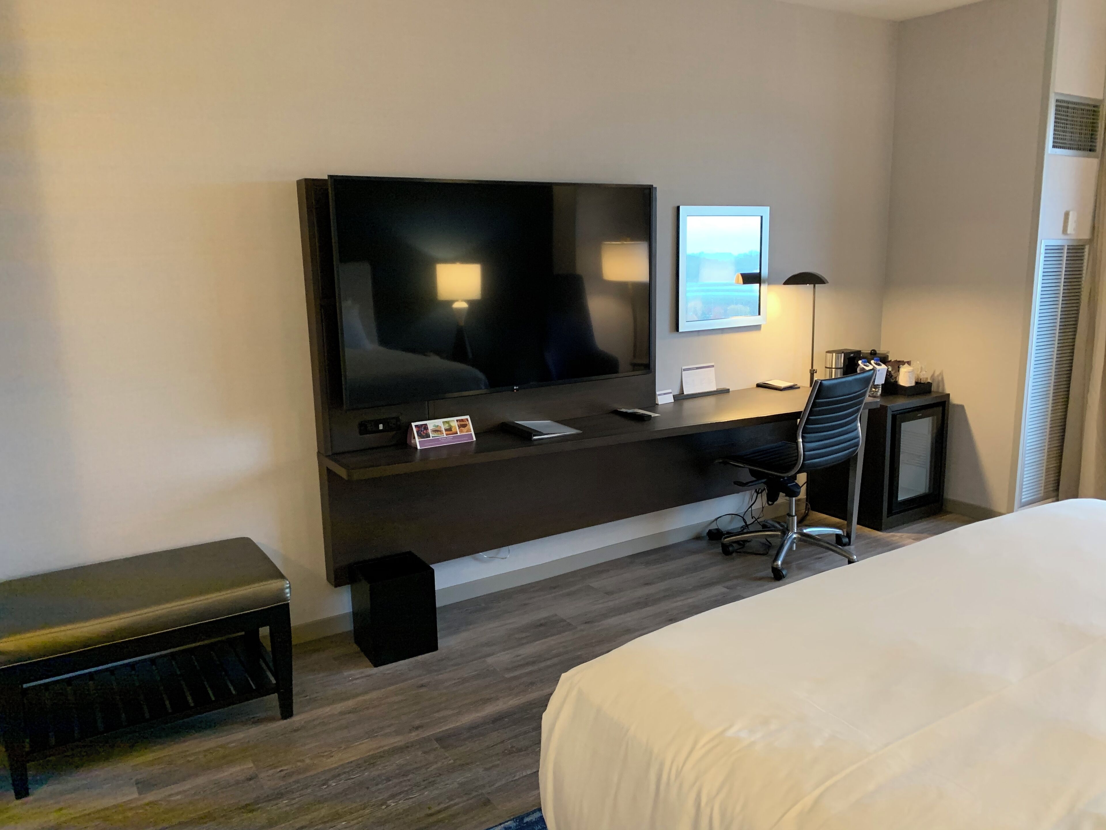 Habitación de hotel con cama, escritorio con computadora, silla, televisor y una mesita.