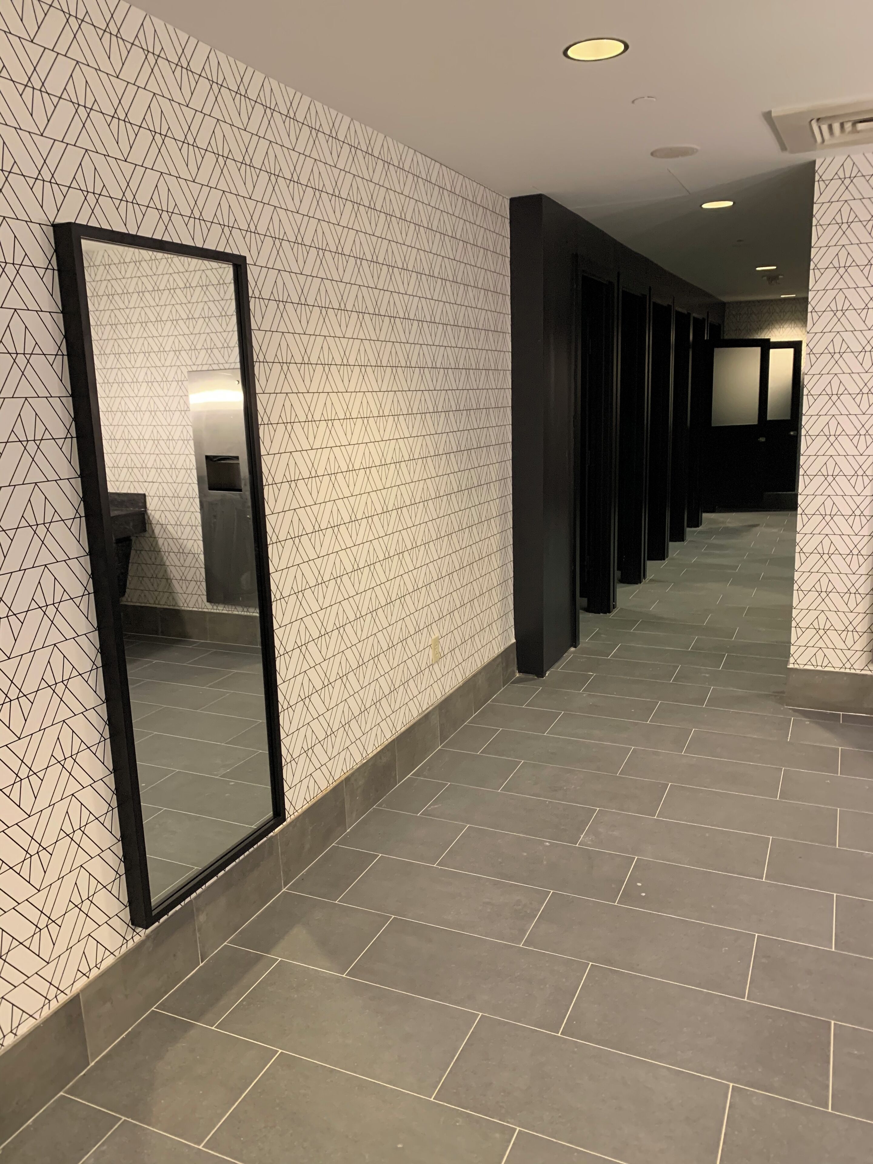 A hallway with patterned walls and a tiled floor, leading to a dark door at the end.