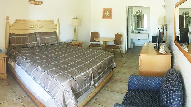 A bedroom with a large bed, a desk with a chair, a small table, a mirror, and a hanging sign.
