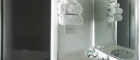 A bathroom with a sink, mirror, and towels stacked on the wall.
