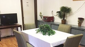 A conference room with a white table, four chairs, a television on a desk, and potted plants.