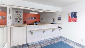 Una zona reception con una scrivania in legno chiaro, un orologio e una parete decorata con quadri.