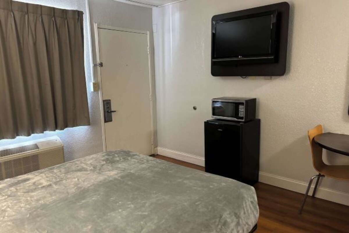 A hotel room with a bed, a TV, a small desk with a chair, and a window with curtains.