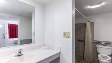 A bathroom with a white sink, mirror, and toilet. There is a shower area with a beige curtain.