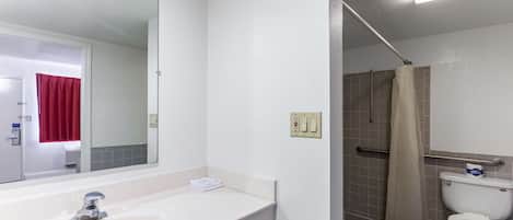 A bathroom with a white sink, mirror, and toilet. There is a shower area with a beige curtain.