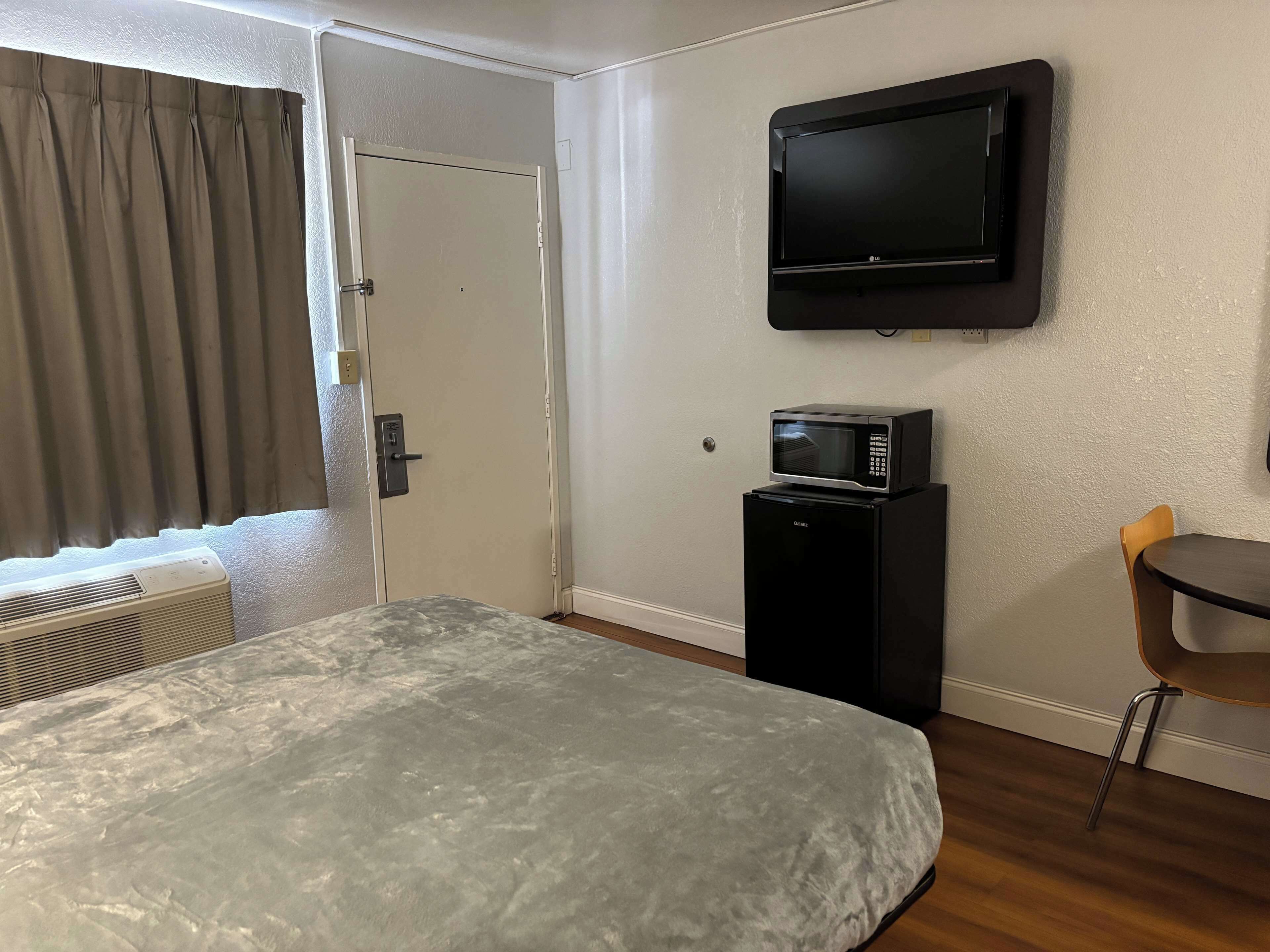 A hotel room with a bed, a television mounted on the wall, a microwave on a small cabinet, and a chair.