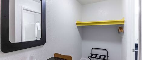 Una habitación pequeña con una mesa redonda, una silla, un espejo, un estante y un perchero.