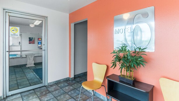 Un'area della reception di un hotel con un cartello 'No Smoking', un cartello 'Motel 6' e una scrivania con una pianta in vaso.