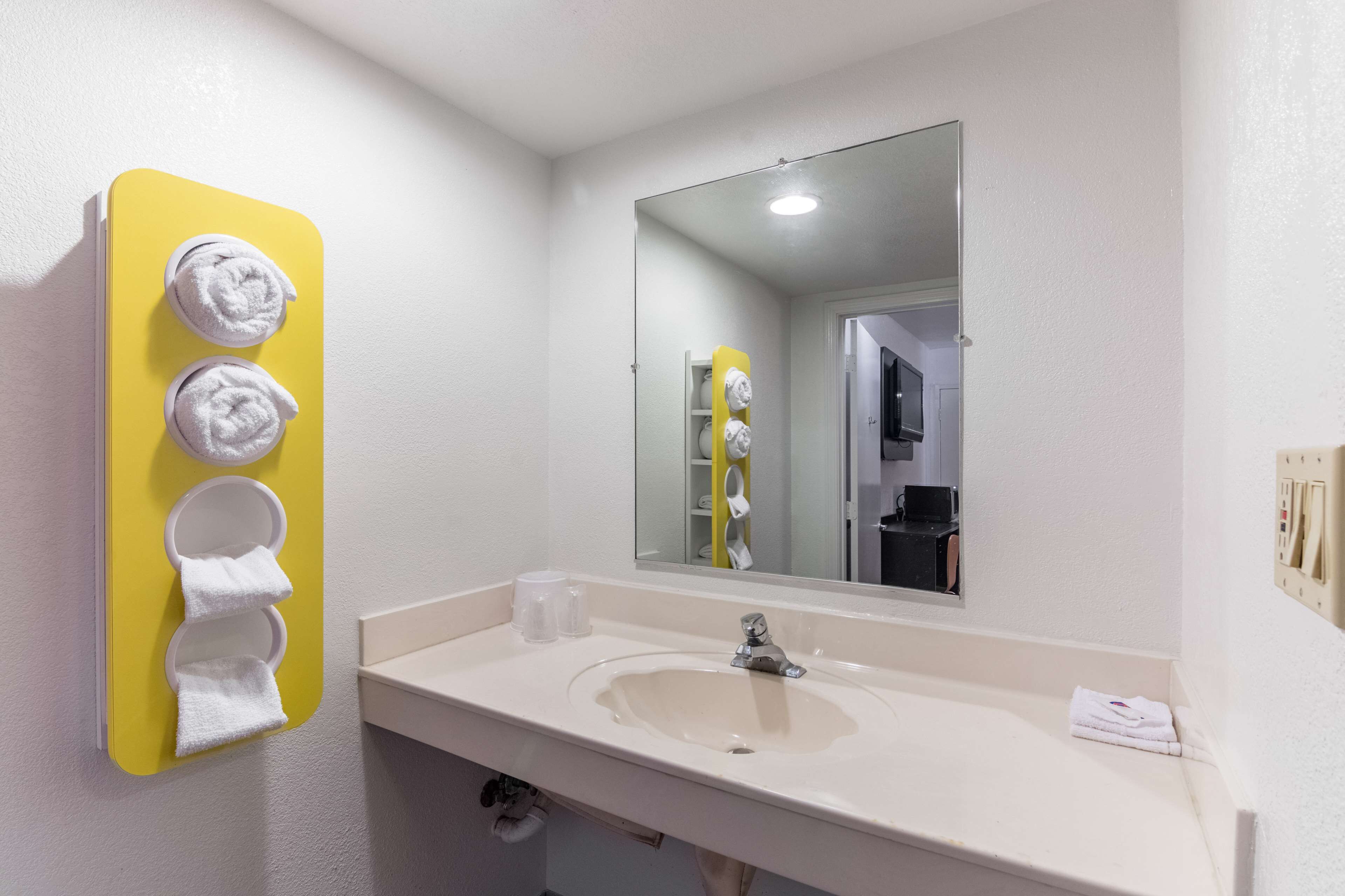 A bathroom with a yellow towel rack holding four towels, a sink with a mirror above it, and a white wall.