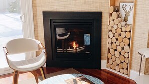 Una sala de estar con chimenea, un sillón, una mesa de centro redonda y un leñero.