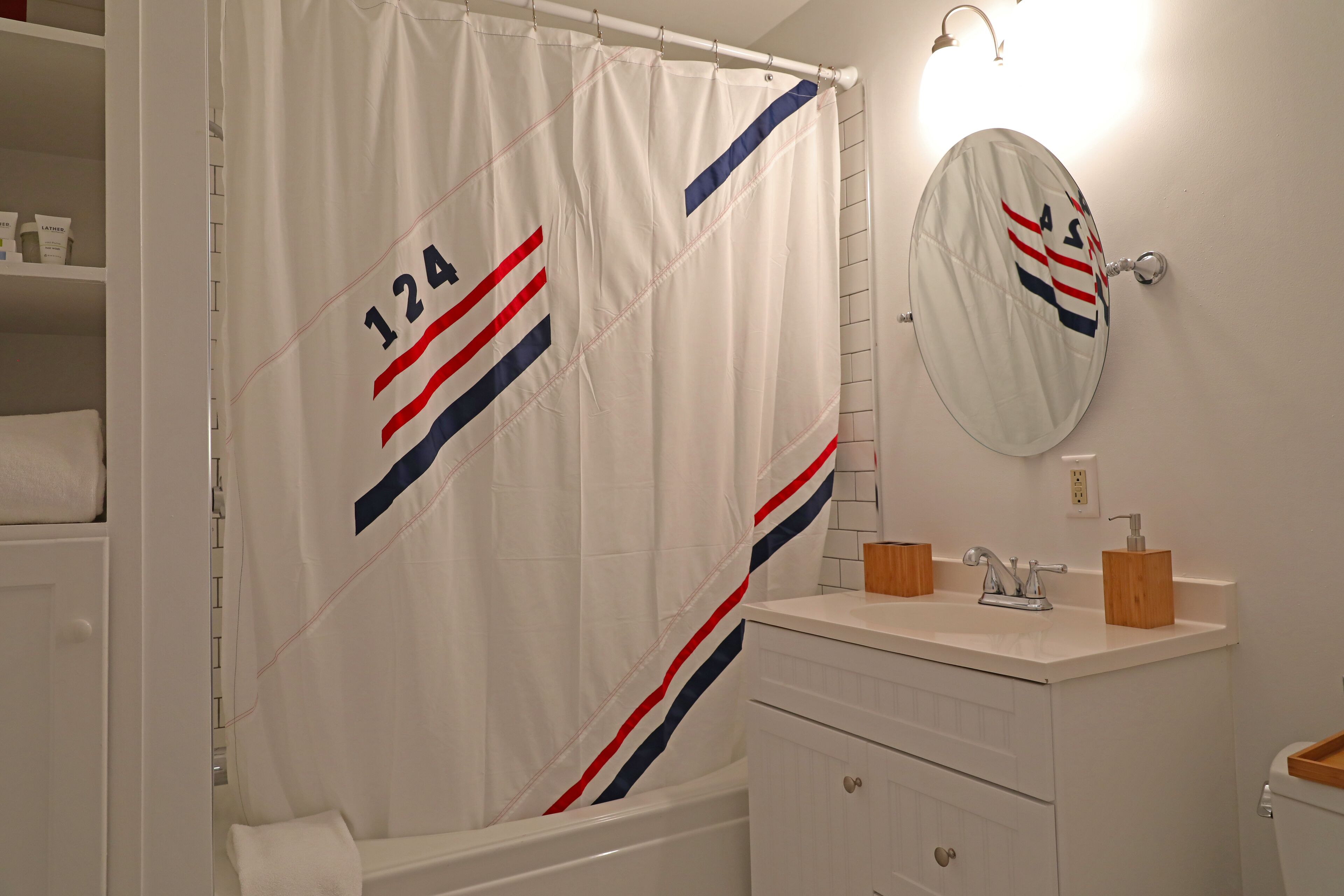 A bathroom with a shower curtain featuring a number and stripes, a mirror, a sink with a soap dispenser, and a toilet.