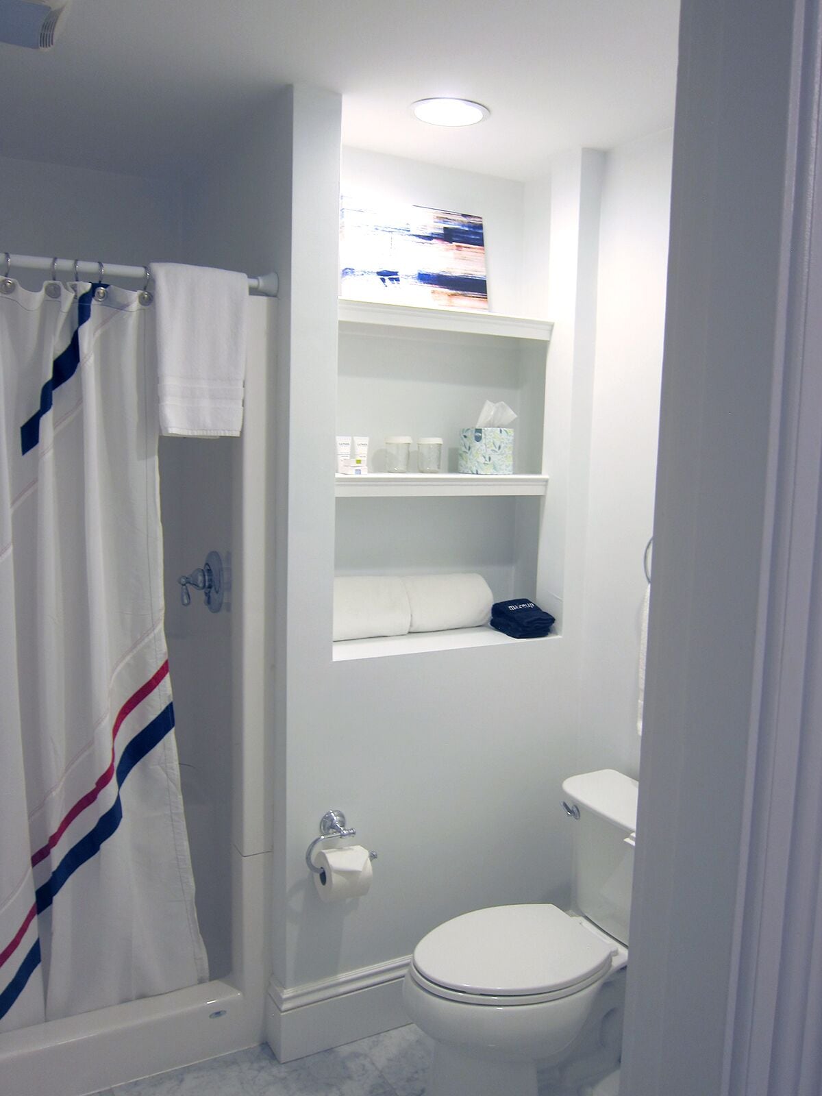Un baño pequeño y funcional con inodoro blanco, cortina de ducha y estante con artículos de tocador.