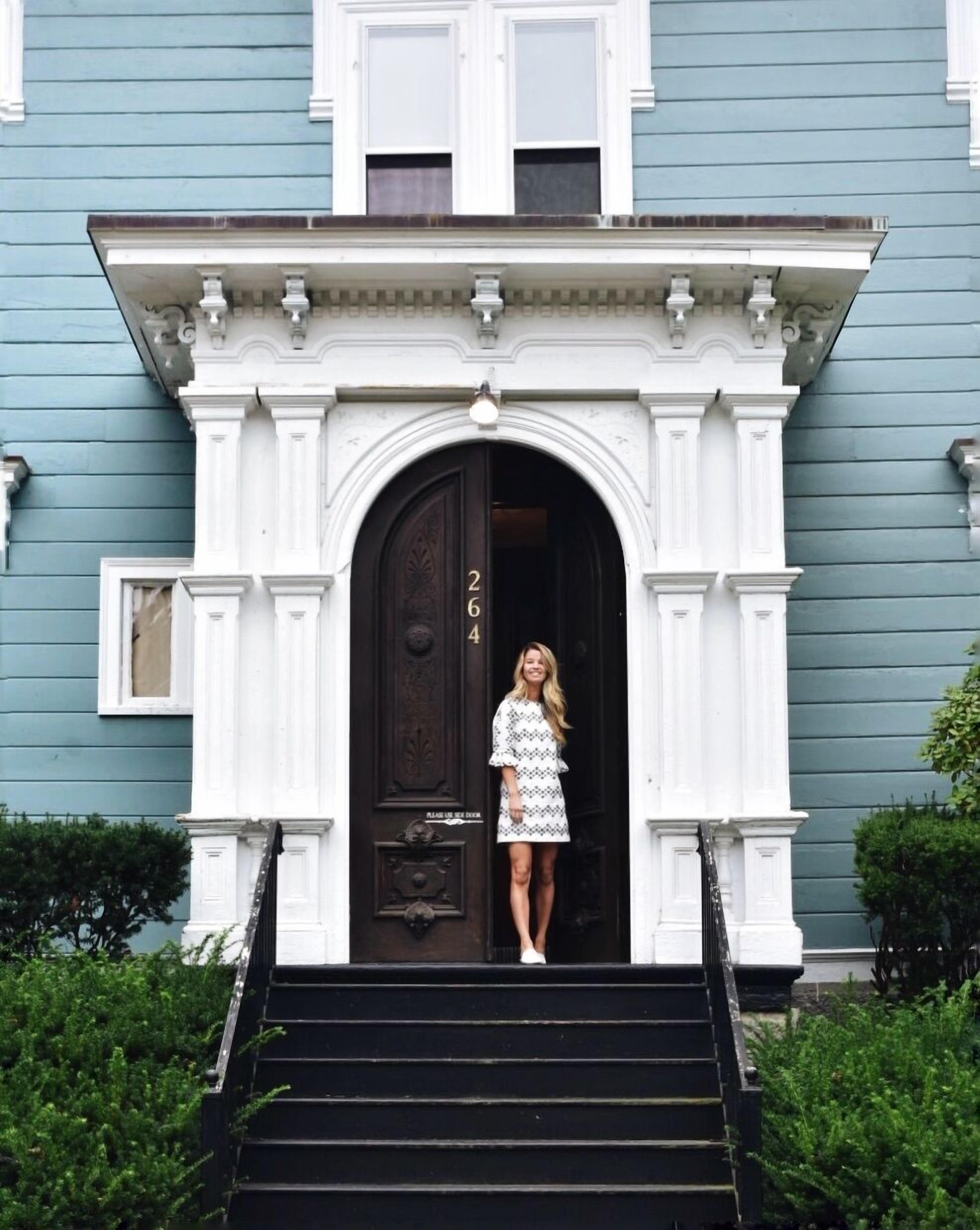 A woman standing at the entrance of a house with a black door and the number 264.
