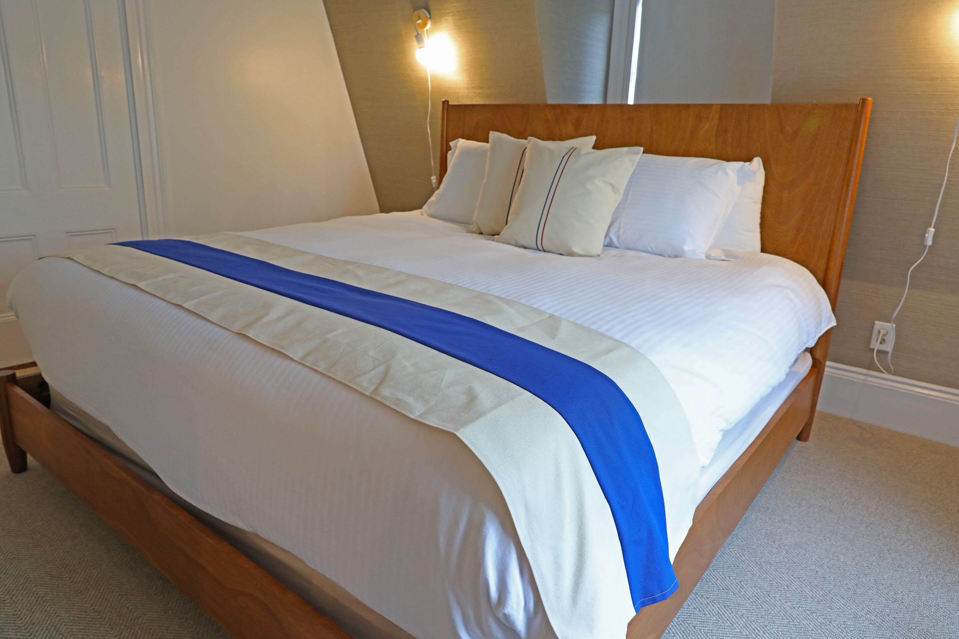 Een netjes opgemaakt bed met een houten hoofdbord, wit beddengoed en een blauw accent.