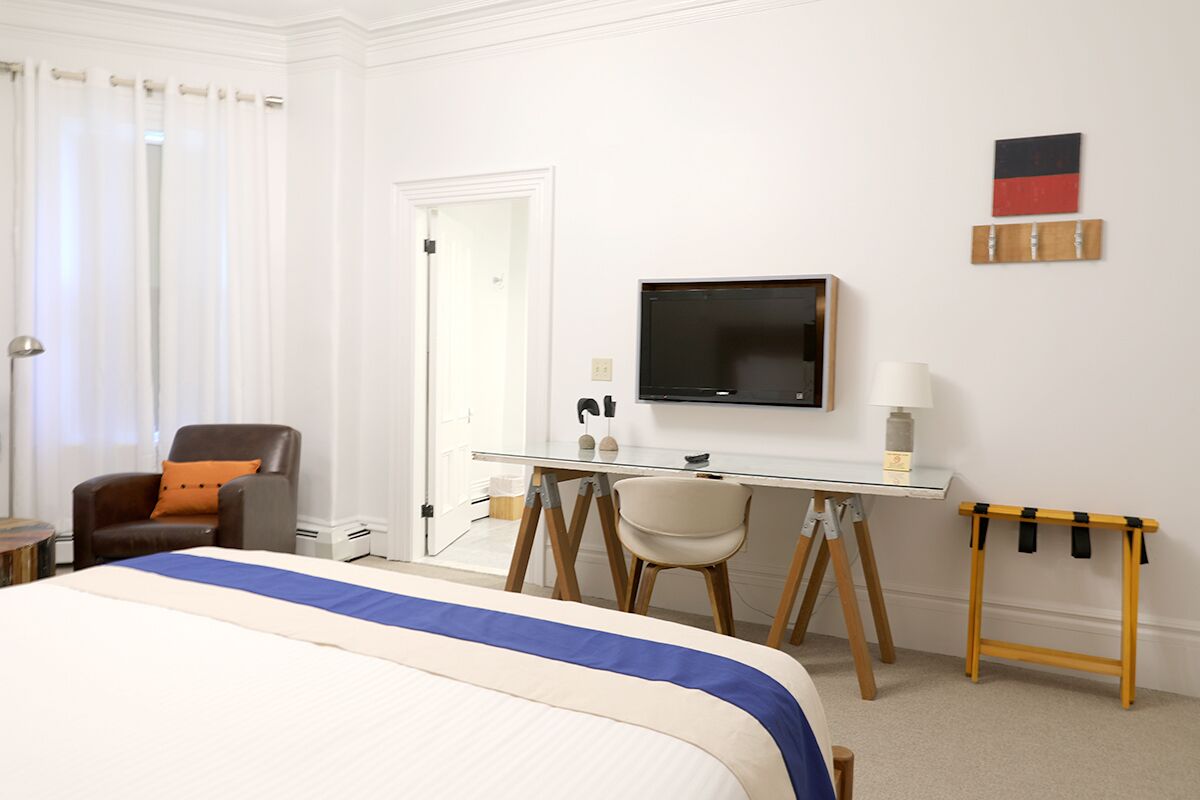 A hotel room with a bed, a desk, a chair, a television, and a small table.