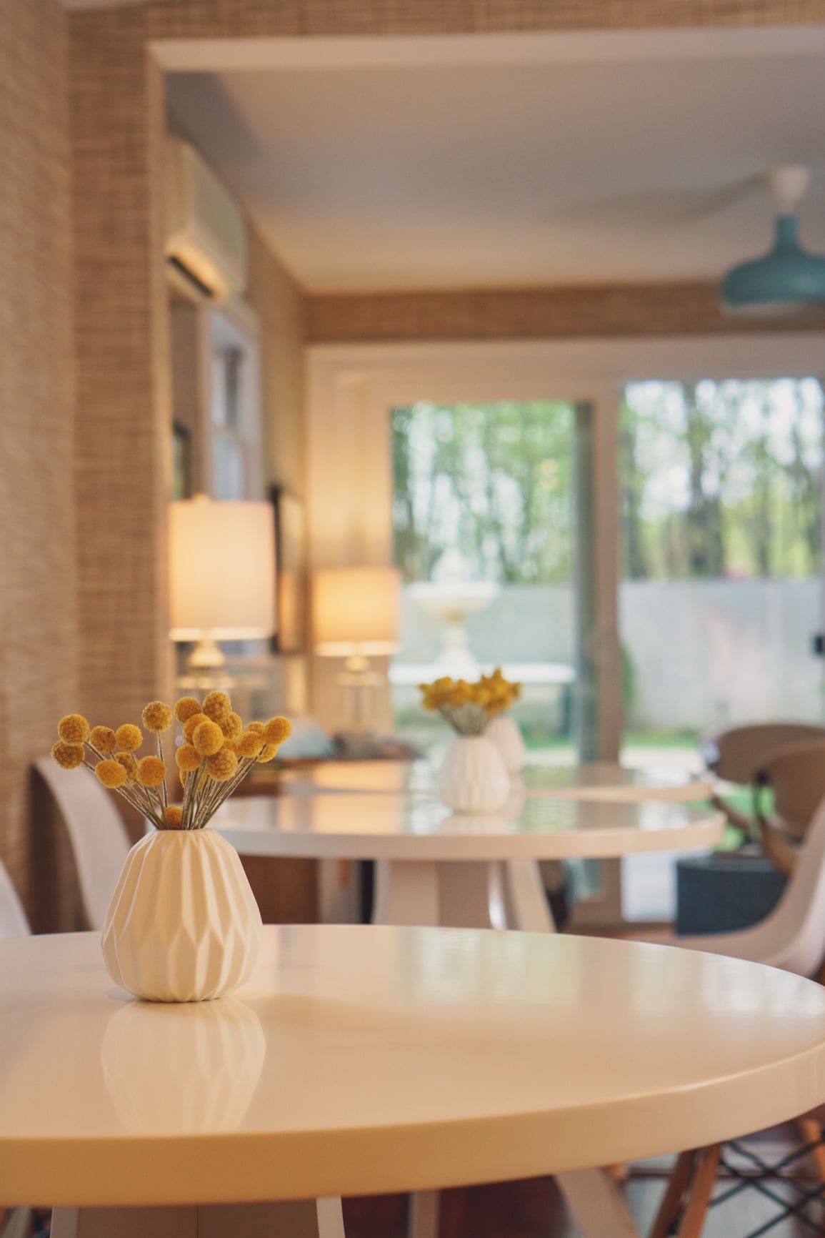 Un coin repas avec une table ronde, un vase rempli de fleurs jaunes et une vue sur l’extérieur.
