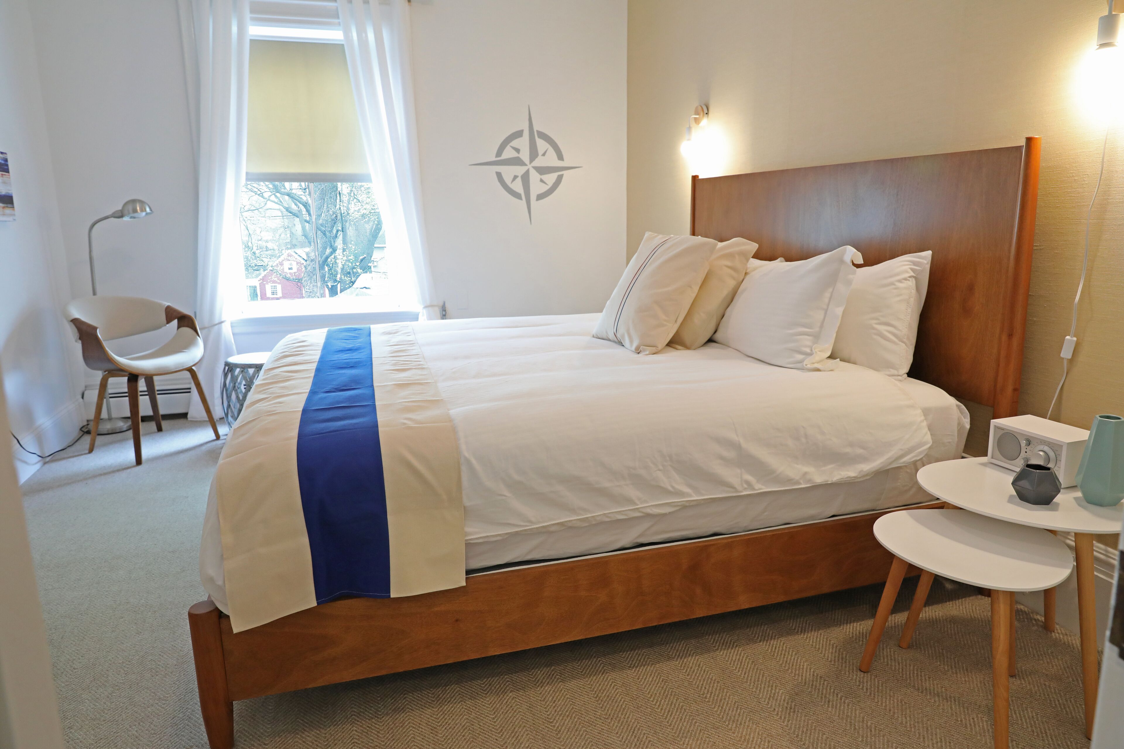 A neatly made bed with a wooden headboard, a bedside table with a lamp, and a window with curtains.