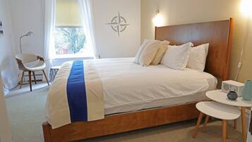 A neatly made bed with a wooden headboard, a bedside table with a lamp, and a window with curtains.