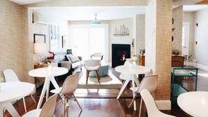 Una sala de estar moderna con chimenea, un comedor con mesas y sillas redondas, y una cocina visible al fondo.