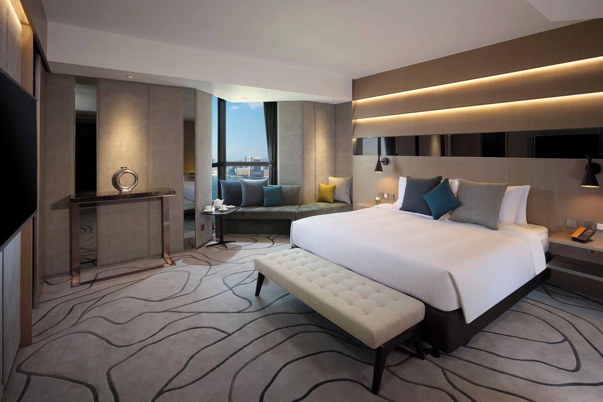 Quarto de hotel moderno com uma cama grande, um banco, uma escrivaninha e vista para a cidade.