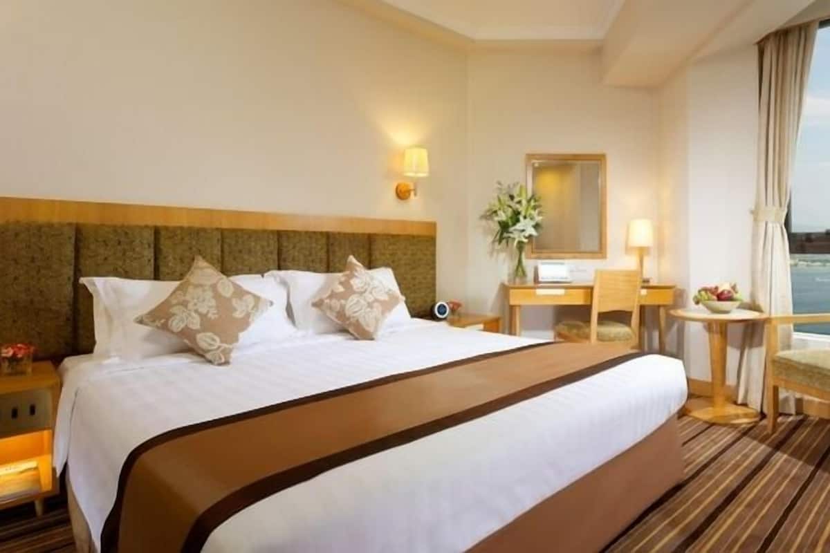 Ett hotellrum med en stor säng, ett skrivbord, en stol, en spegel och utsikt över stadsbilden.