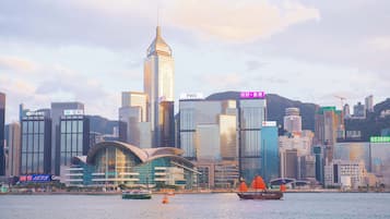 A city skyline with modern buildings, a prominent skyscraper, and a body of water with boats.