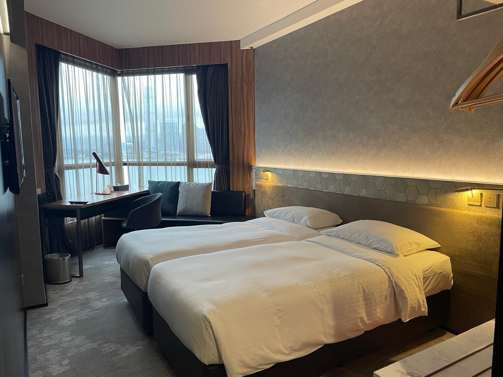 Une chambre d’hôtel avec deux lits, un bureau et une grande fenêtre avec des rideaux.