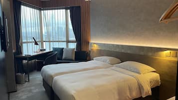 A hotel room with two beds, a desk, and a large window with curtains.