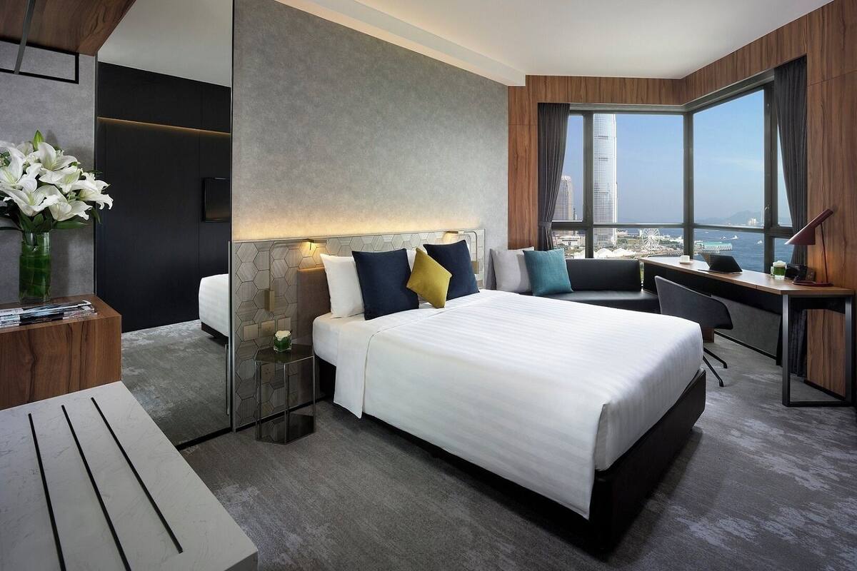 Quarto de hotel moderno com uma cama grande, uma escrivaninha e vista para a paisagem urbana.