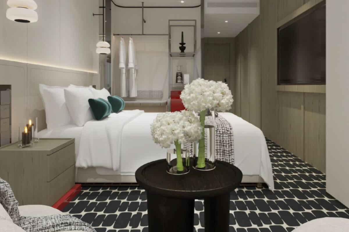Quarto de hotel moderno com uma cama bem arrumada, uma mesinha de cabeceira com velas e uma mesa redonda com flores brancas.