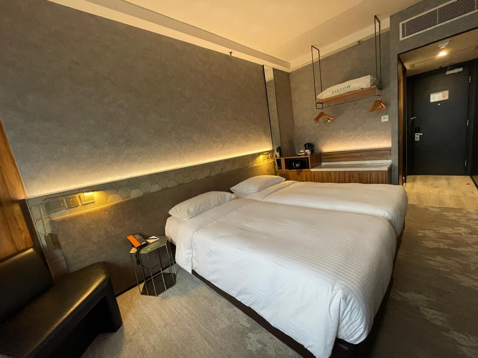 A modern hotel room with a large bed, bedside tables, a bench, and a built-in bench along the wall.