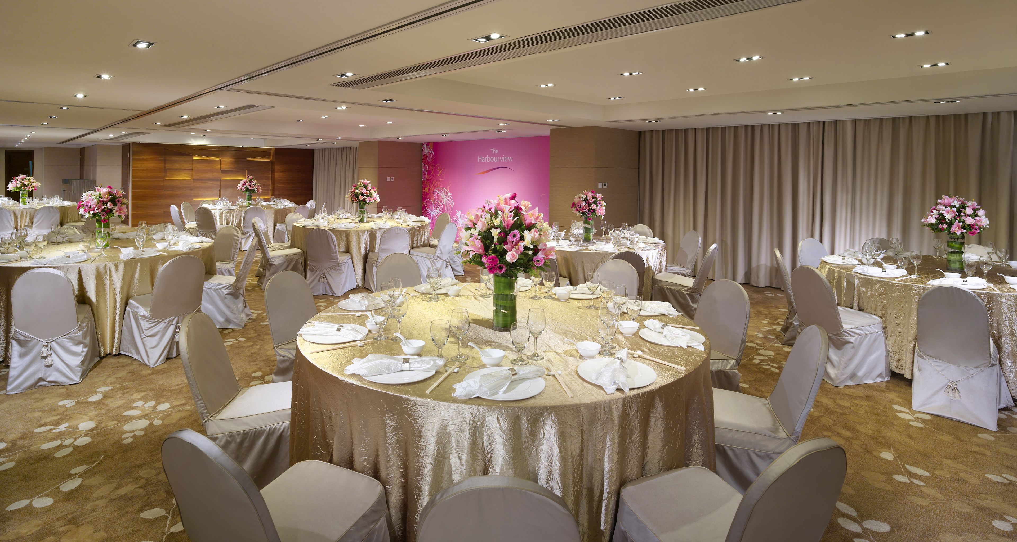 Un salón de banquetes con mesas redondas dispuestas para comer, cada una con mantel blanco y centros de mesa florales.