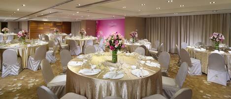 A banquet hall with round tables set for dining, each with white tablecloths and floral centerpieces.
