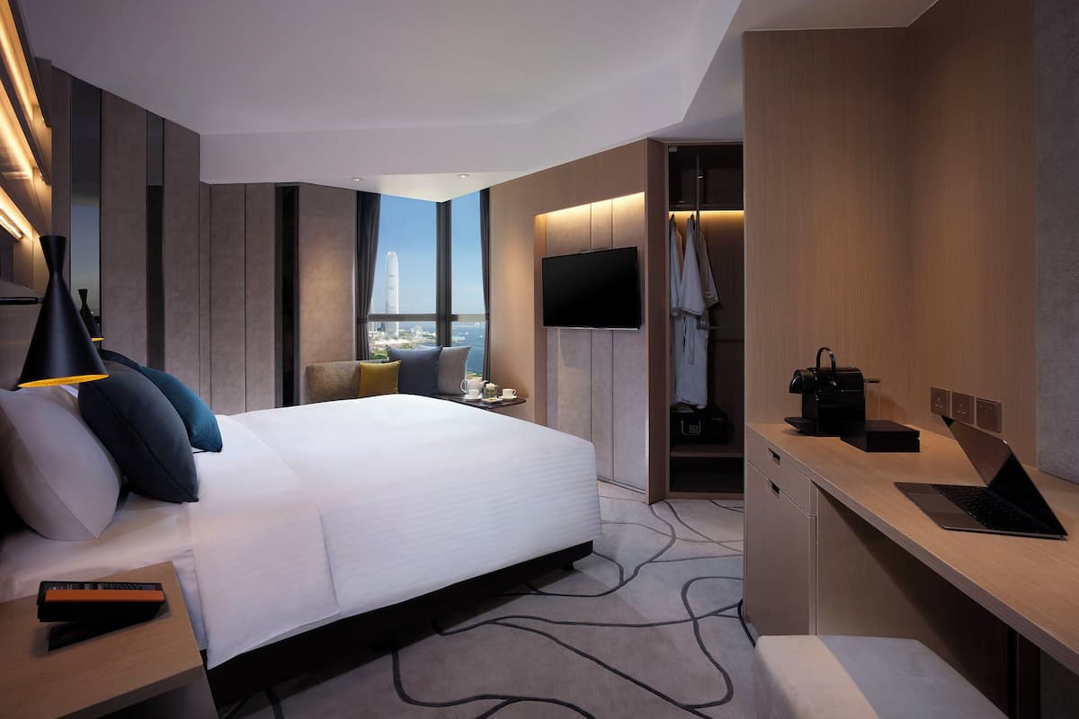 Quarto de hotel moderno com uma cama grande, uma escrivaninha com um laptop, uma televisão e vista para a paisagem urbana.