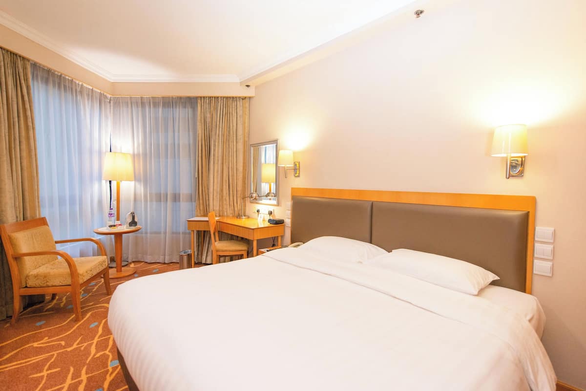 Ett hotellrum med en stor säng, ett skrivbord med en stol, en lampa och en spegel.
