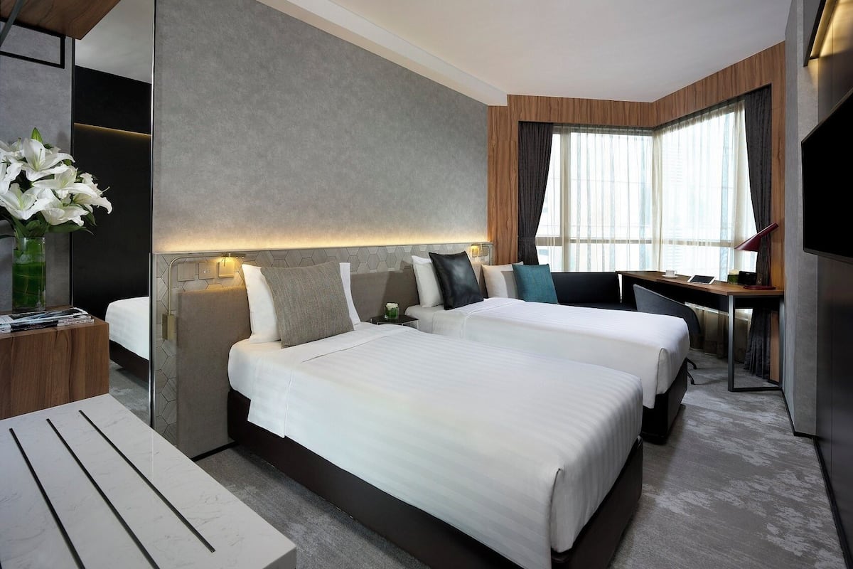 Quarto de hotel com duas camas, uma mesa de trabalho e uma janela grande com cortinas.