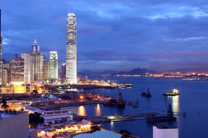 A city skyline with prominent skyscrapers, a harbor with boats, and construction cranes.