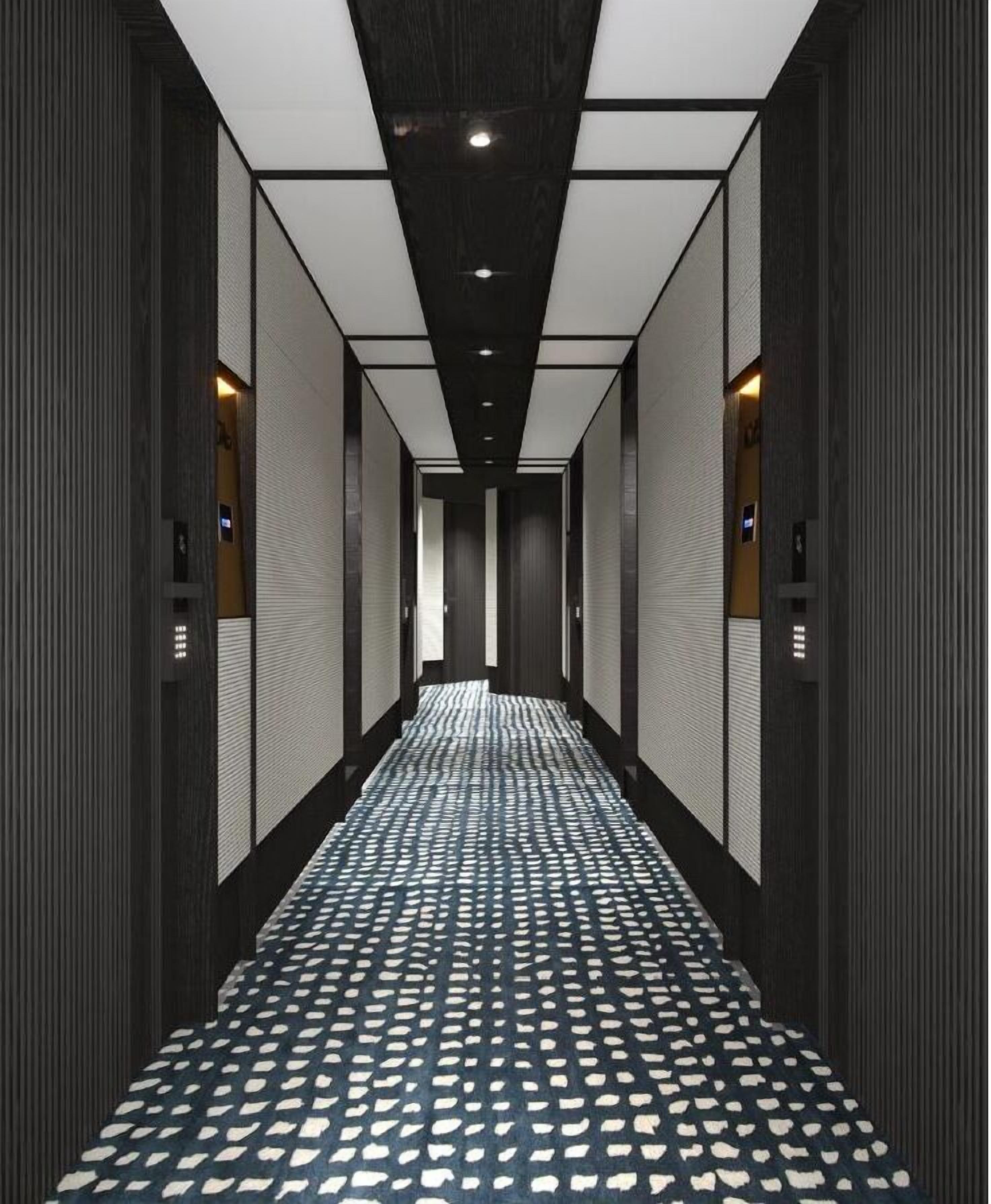 Un pasillo largo y estrecho con piso estampado, paredes con líneas verticales e iluminación en el techo.