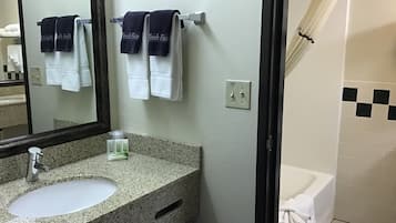 A bathroom with a granite countertop sink, a mirror, two towels hanging on a rack, a fan on the wall, and a shower area with a white curtain.