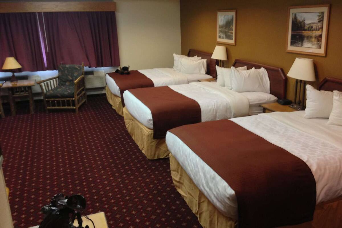 A hotel room with three beds, a desk, and a chair.