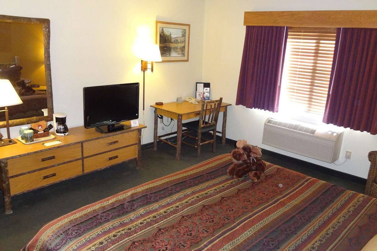A hotel room with a bed, a desk, a chair, a television, a lamp, a window with curtains, and a radiator.