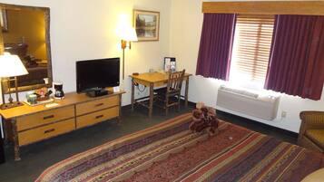 Habitación de hotel con cama, escritorio, silla, televisor, lámpara, ventana con cortinas y radiador.
