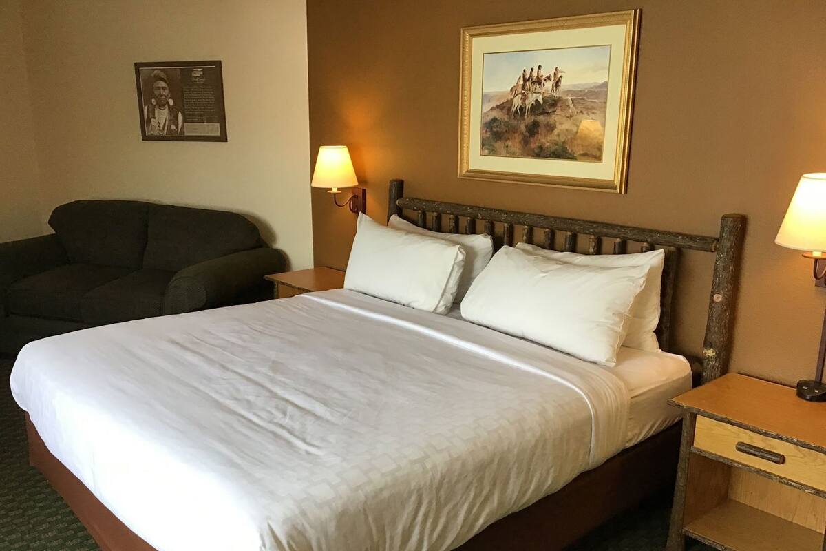 A hotel room with a large bed, two bedside tables, a chair, and a wall-mounted painting.