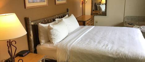 Una habitación de hotel con una cama grande, una mesita de noche con lámpara, un aparador y dos cuadros enmarcados en la pared.