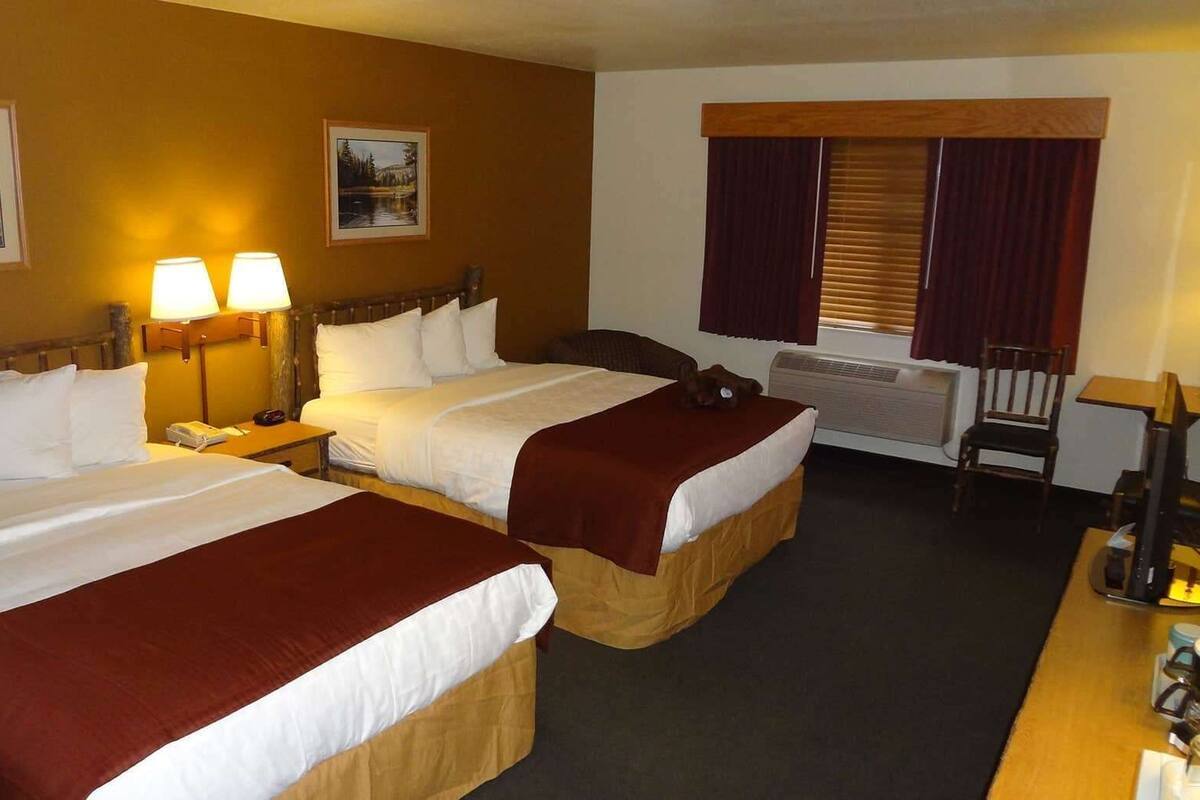 A hotel room with two beds, a desk, a chair, a lamp, and a window with curtains.