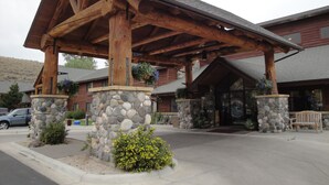 A lodge with a stone facade, wooden beams, and a covered entrance. - AmericInn by Wyndham Cody (Cody)