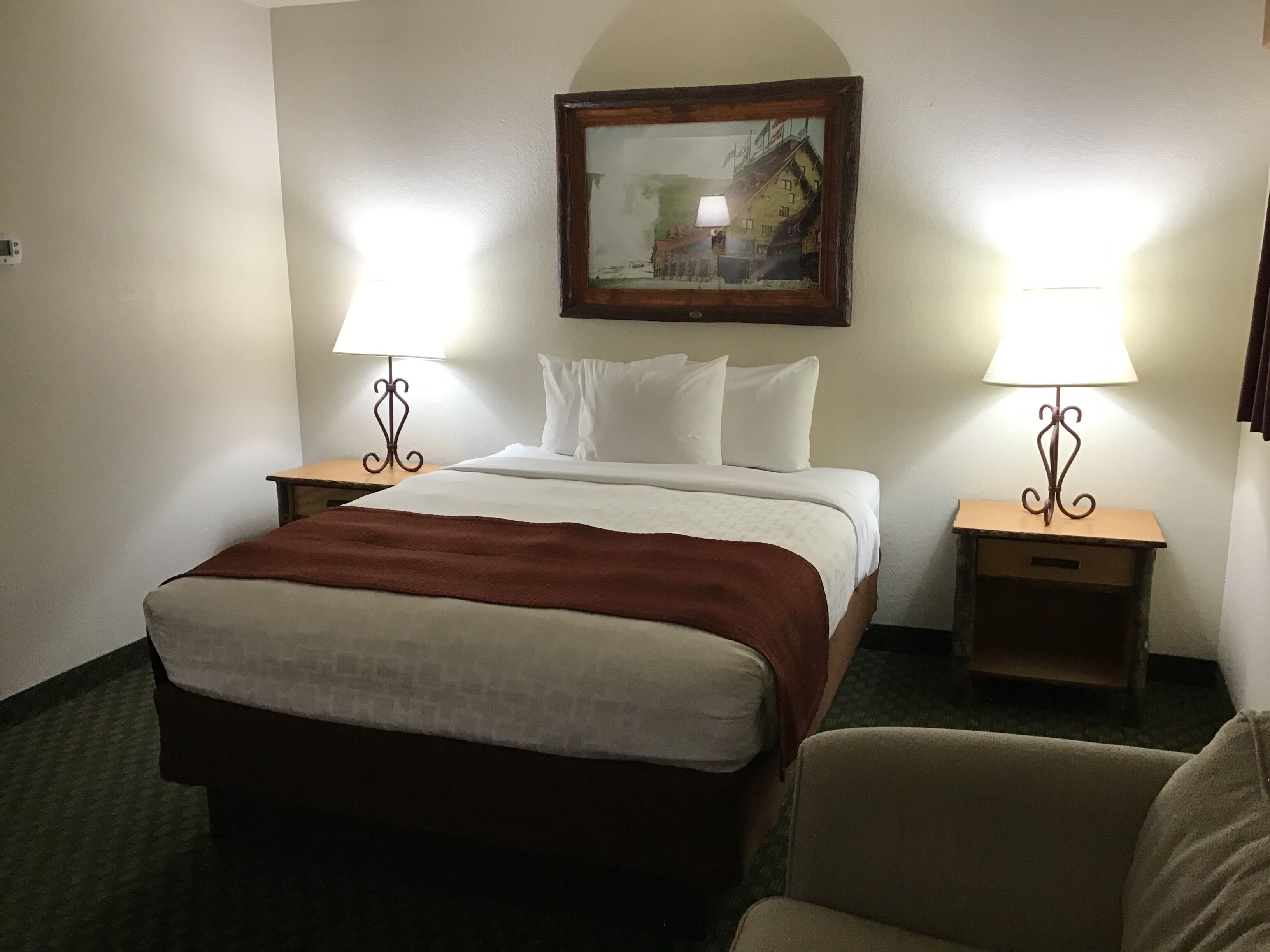 A hotel room with a bed, two bedside tables with lamps, a framed picture on the wall, and a chair.