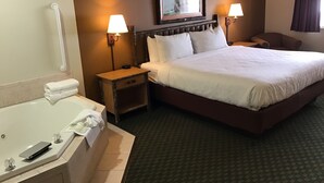 A hotel room with a large bed, two bedside lamps, a nightstand, a chair, a bathroom with a bathtub, and a framed picture on the wall. - AmericInn by Wyndham Cody (Cody)